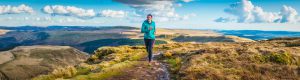 Active teenager trail running along rocky path through grassland high in mountain wilderness. ProPhoto RGB profile for maximum color fidelity and gamut.